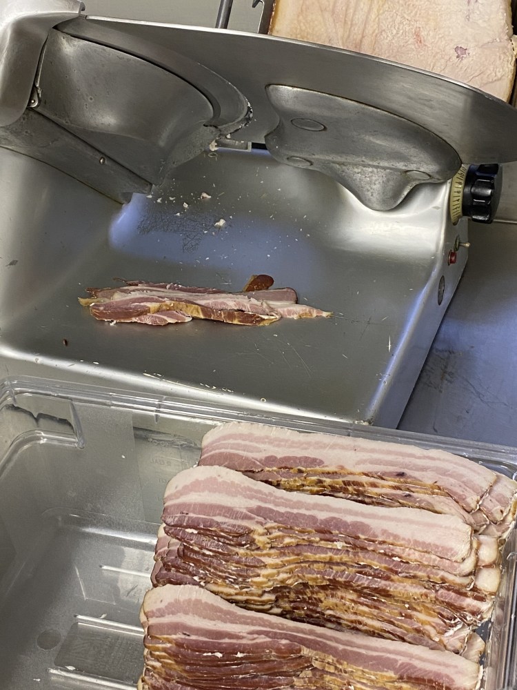 Stacks of fresh cut bacon in front of a deli slicer